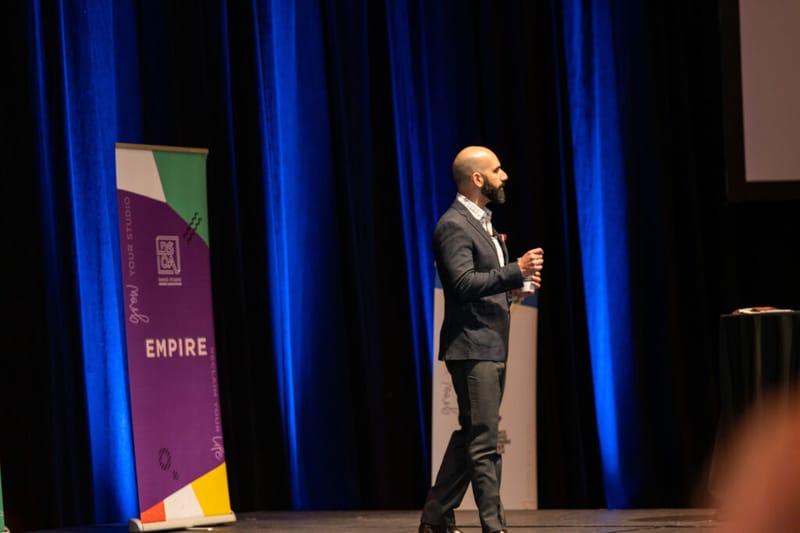 Ayman Al-Abdullah speaking on stage beside a Dance Studio Owners Association Empire banner
